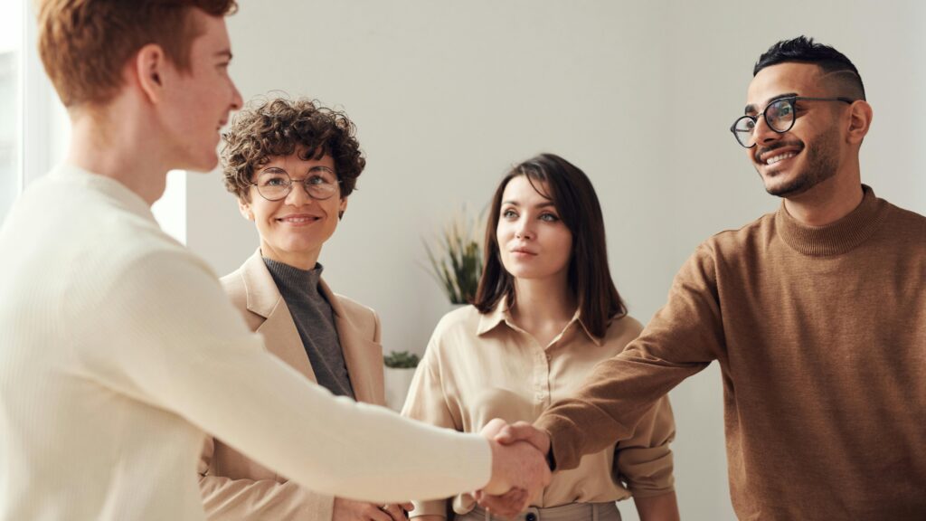 Four colleagues in an office handshake demonstrating teamwork and cooperation.